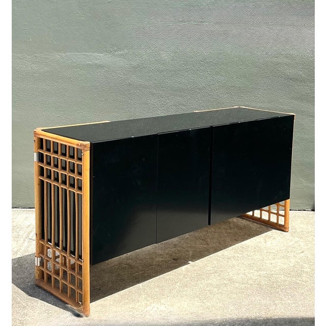 This vintage rattan and lacquered wood sideboard is a sophisticated example of Mid-Century Modern design, blending natural...