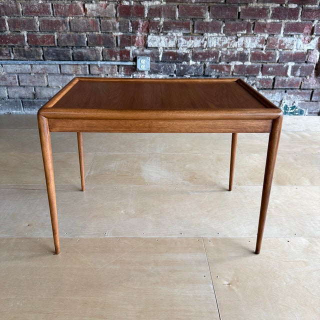 This side table, designed by T.H. Robsjohn Gibbings for Widdicomb, has thin legs with silver metal caps. The rounded...