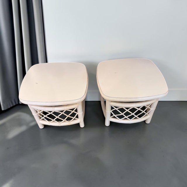 A delightful pair of vintage rattan and wood side tables featuring a soft white painted finish and decorative woven...