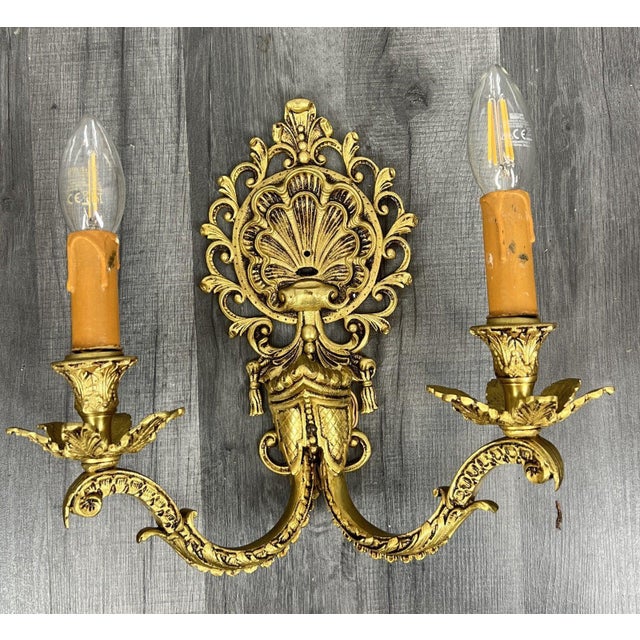 A striking pair of vintage french wall sconces , richly decorated with rococo-style ornamentation and scrolling candle-...