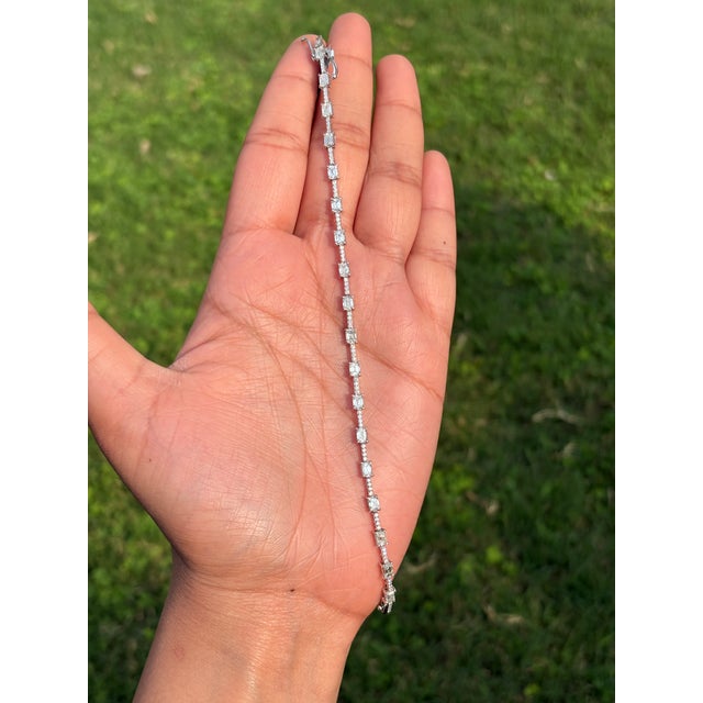 This 3.77 carat natural emerald cut diamond station tennis bracelet is crafted in 14k white gold, emeralds arranged in a...