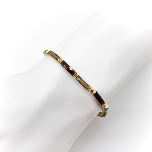 This 14k gold vintage bracelet features alternating garnets and smoky quartz stones in elongated French cuts. The stones...