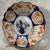 19th century Japanese Imari plate. Scalloped rim, central floral in vase, border interspersed with foliage and landscape...