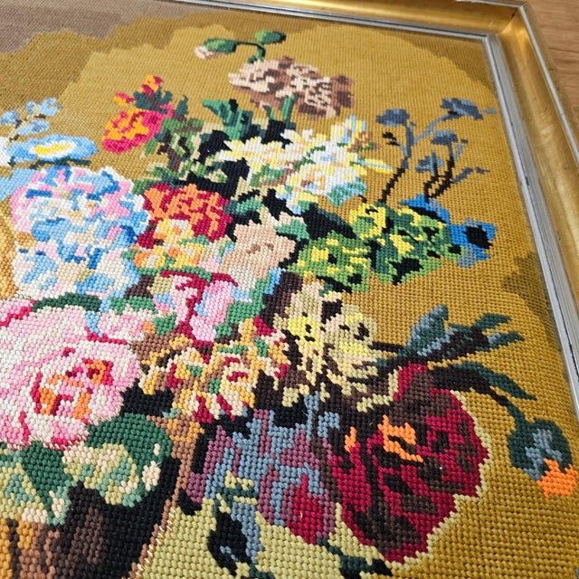 Hand-stitched needlepoint tapestry features a vibrant floral still life arrangement in a classical urn, set against a rich...