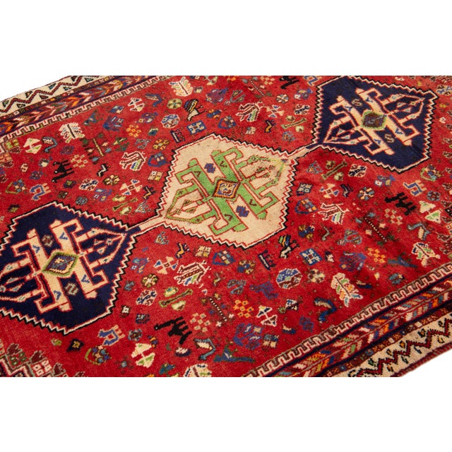 This stunning handmade wool rug showcases a red field adorned with navy blue and multicolored tribal designs. This rug...