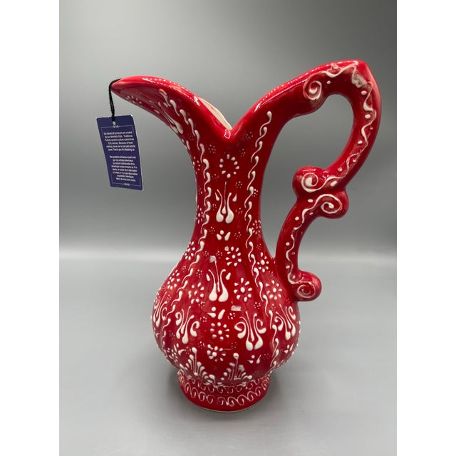 Vintage-style red decorative pitcher with an elegant sculptural silhouette, scrolling handle, flared spout, and raised...