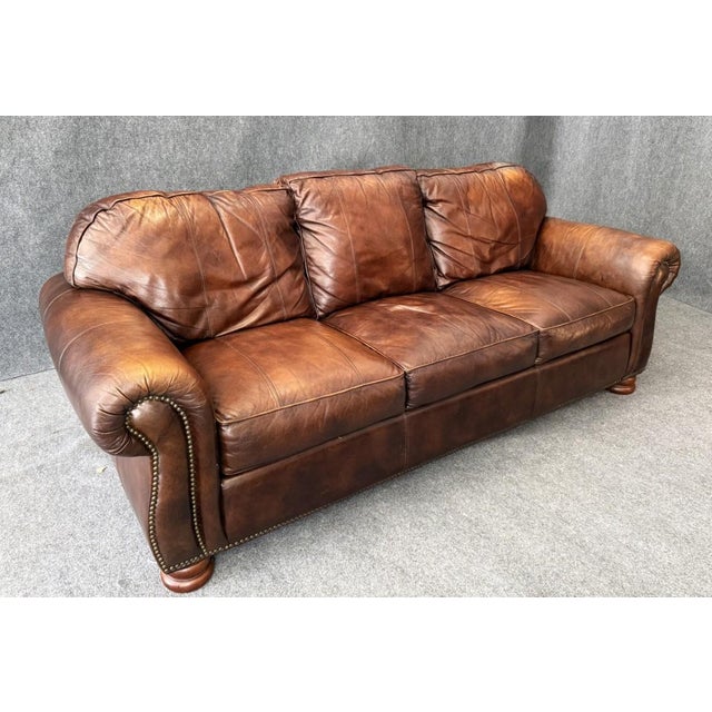 This Thomasville brown leather sofa features a classic three-seat design with generously padded cushions, rolled arms, and...