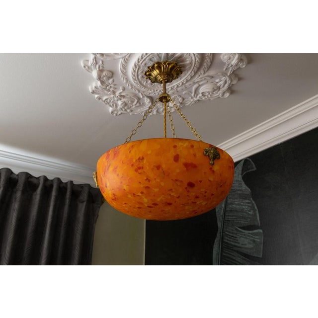 French art deco pendant light from the 1930s, featuring a deep mottled orange glass bowl suspended by sculptural brass...