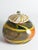 This vibrant, one-of-a-kind lidded vessel features a bulbous, spherical body with a translucent, smoky-grey base that is...