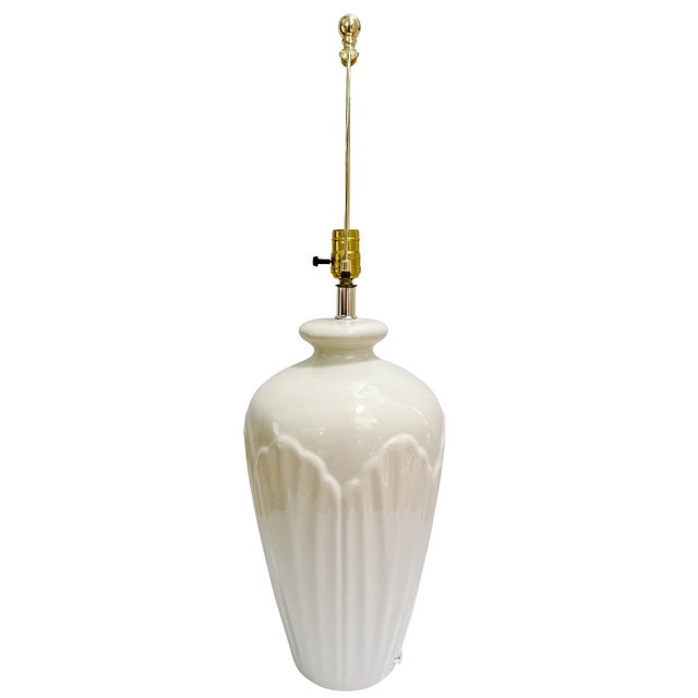 An elegant vintage table lamp featuring a luminous cream-colored ceramic body with sophisticated architectural detailing....