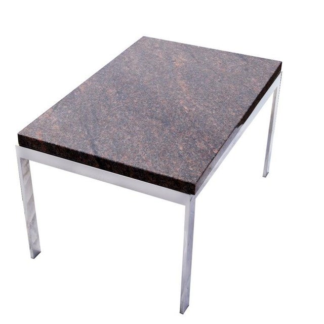 A mid century modern rectangular coffee table with a chrome base and rose granite top