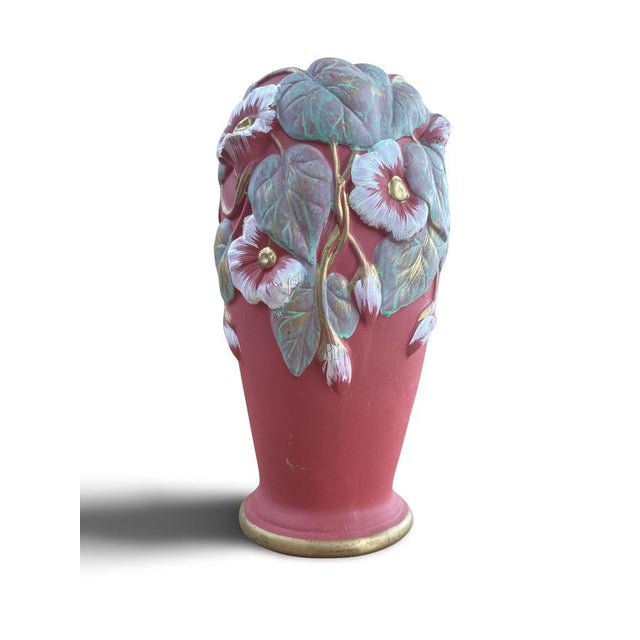 A ceramic vase with a slightly flared body, resting on a rimmed base. The body is covered with a matte pink slip, upon...