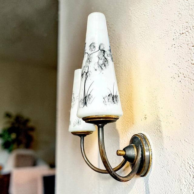 A refined pair of vintage double wall sconces from the 1960s. The lamps are made of brass, and crowned with white glass...