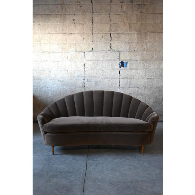 An Italian mid century modern clam shell sofa with a striking silhouette. The arched channel back and curved seat are...