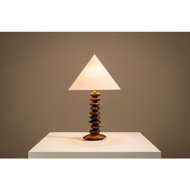 There is a quiet rhythm to this table lamp, created through repetition rather than ornament. Its stacked wooden body gives...