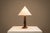 There is a quiet rhythm to this table lamp, created through repetition rather than ornament. Its stacked wooden body gives...