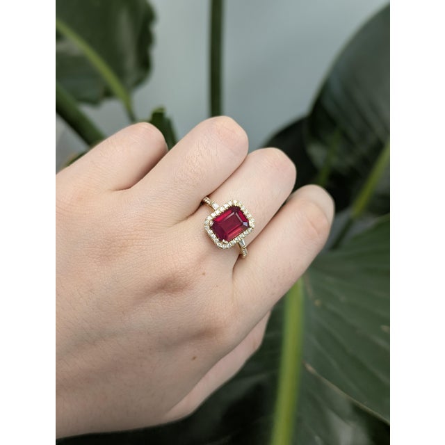 Designed to stand out, this 2.6-carat emerald-cut ruby ring features a rich red center stone accented by earth-mined round...