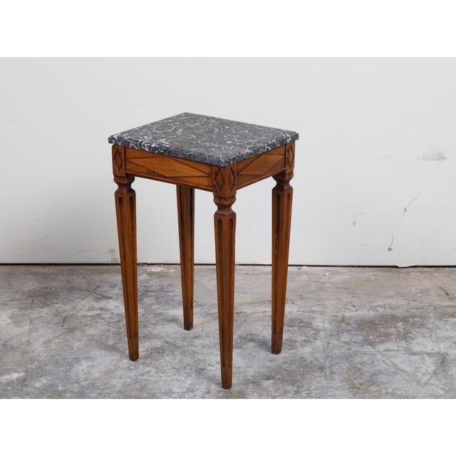 A French Neoclassical style wooden side table from the 19th century, with grey marble top and fluted legs. Created in...