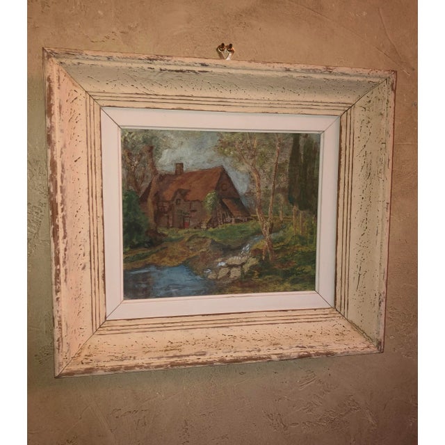 A vintage French landscape oil painting with a thatched roof cottage in the woods near a stream. In a distressed wooden...