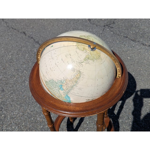 A vintage, tan-colored terrestrial globe mounted on an exquisite bamboo style wooden stand.
