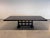 A striking dining table with a strong architectural presence. The thick top is in a deep, dark-stained oak that lets the...