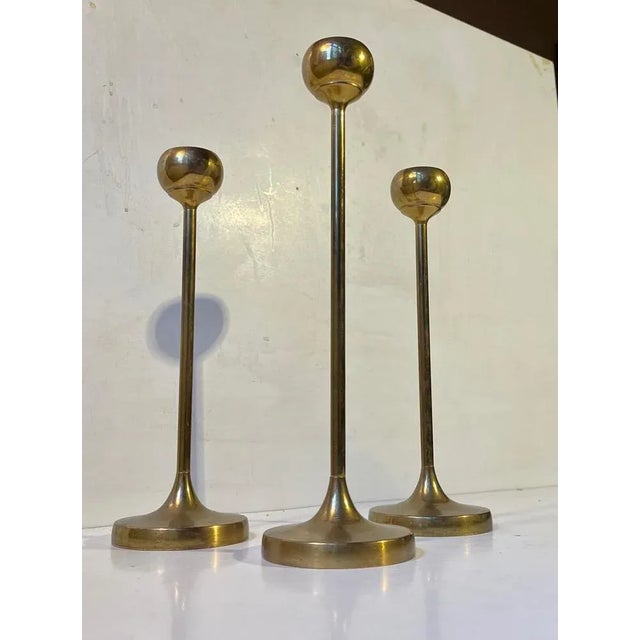 A trio of tulip shaped brass candlesticks designed and manufactured in Scandinavia during the 1960s ina style reminiscent...
