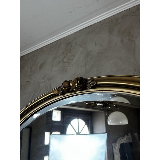 Elegant antique oval mirror in wood and gilt stucco, adorned with a delicate relief of roses and foliage arranged around...