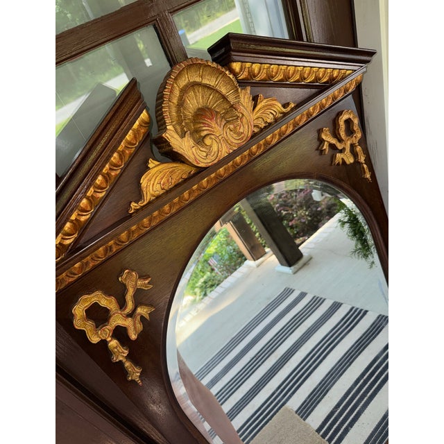 Elegant Henredon wall mirror has a dark wood frame with an arched top and ornate gold-painted carvings. The frame is...