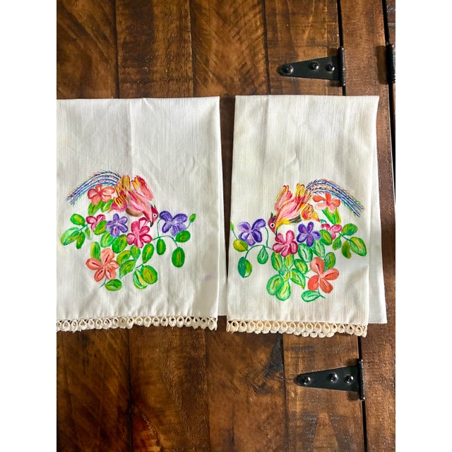 two white hand towels decorated with colorful hand-painted designs, Each towel features an identical artwork theme, with...