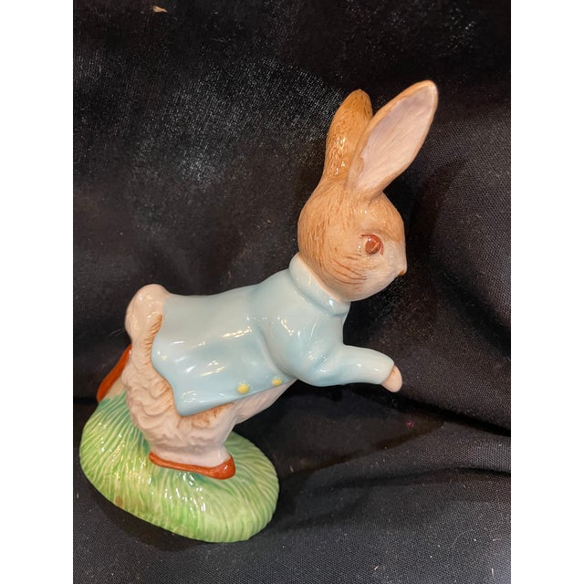 A ceramic figurine of Peter Rabbit in a blue jacket, running on a green base. The figurine is part of a collection...