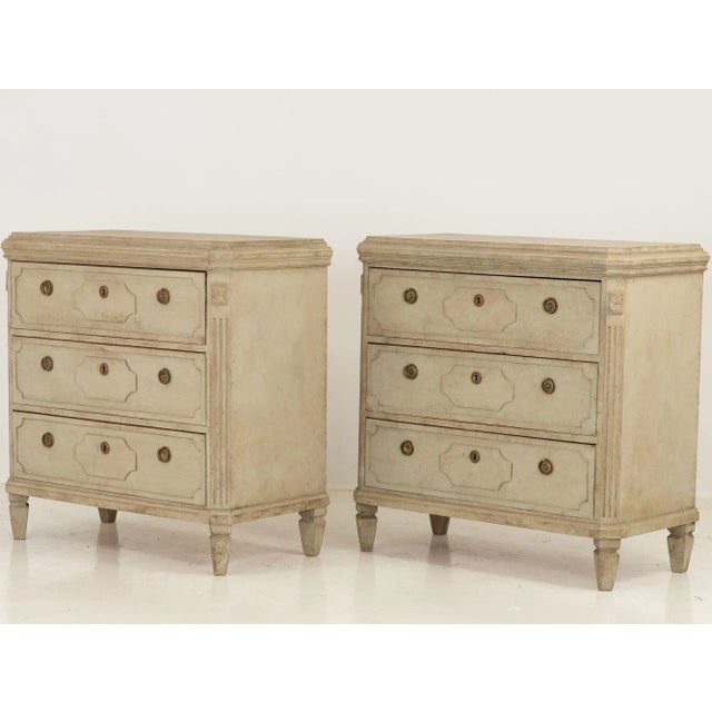 A pair of Swedish Gustavian-style reproduction chests of drawers. Each commode has three drawers with brass ring pulls and...