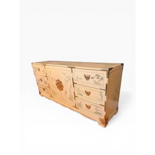 Vintage chinoiserie dresser featuring a cream lacquered finish with hand-painted bird and landscape motifs across the...