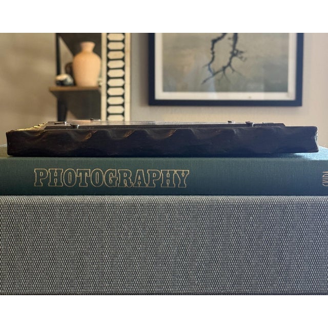 A sculptural hand-carved wood picture frame featuring deeply incised linear detailing, an irregular organic edge, and a...
