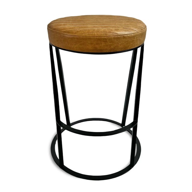 Round warm tan top grain leather seat backless counter stool with black iron base. Slightly aged leather finish with...