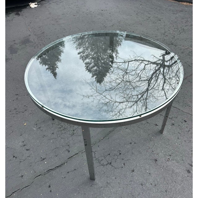 This round, 1970’s modern-style table featuring a clear glass tabletop set on a chrome frame. The tabletop is circular,...