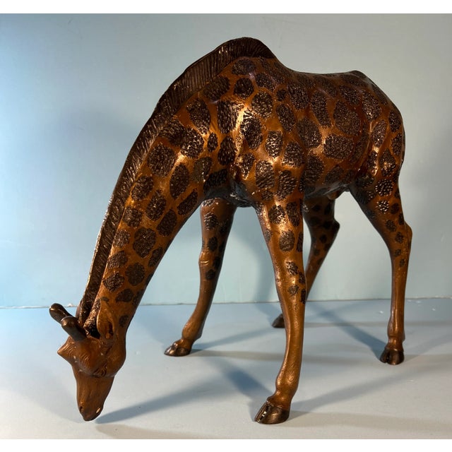 This majestic bronze sculpture intricately portrays the grace and beauty of a giraffe in a natural, feeding pose. The...