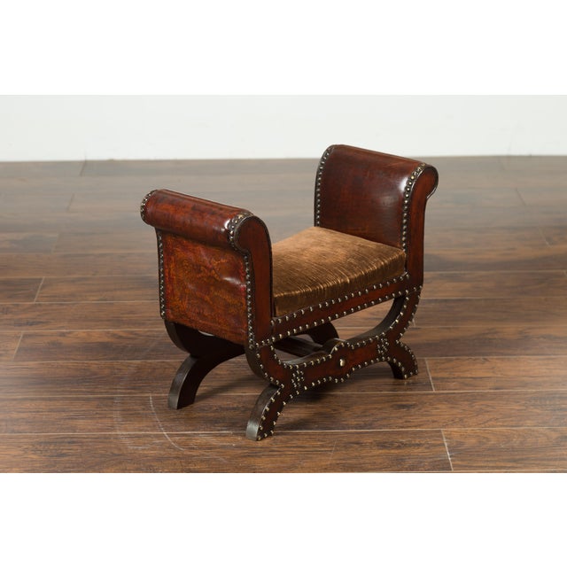 A petite English leather-bound stool from the early 20th century, with out-scrolling arms and nailheads. Created in...