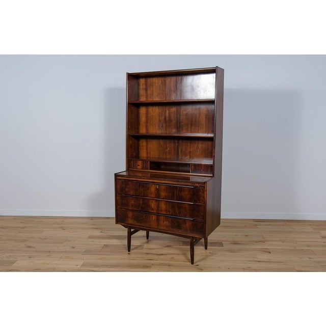 This Mid Century shelf in rosewood was manufactured in the Denmark the 1960s. This mid century shelf has 3 shelves and two...