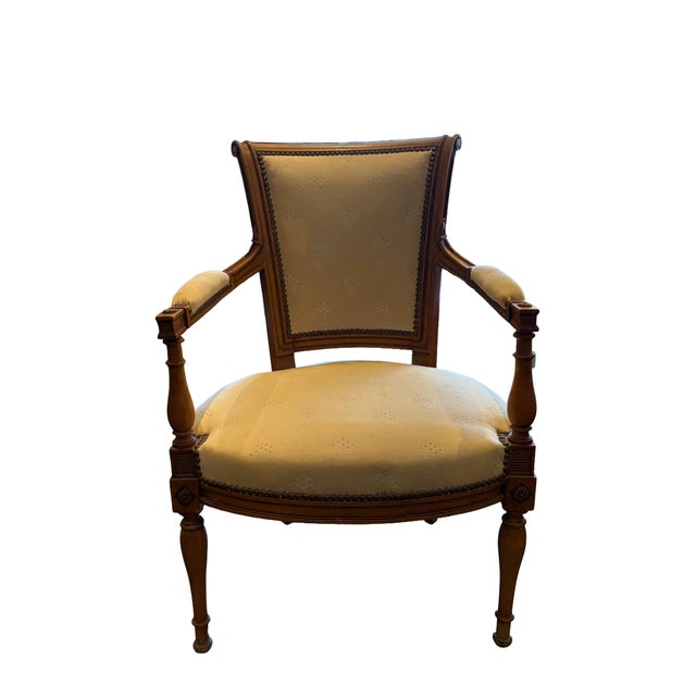 Pair of Neoclassical/Louis XVI-style armchairs featuring carved warm wood frames with scrolled backs, padded armrests, and...