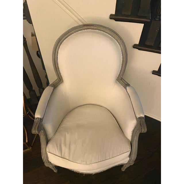 An elegant pair of Louis XVI–style bergère armchairs with oval backs, fluted legs, and graceful French neoclassical lines....