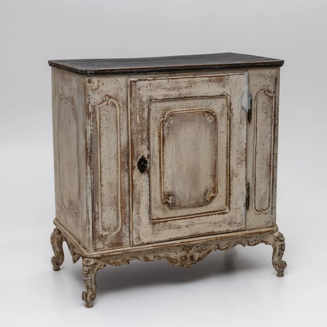 Single-door Baroque half cabinet featuring a serpentine carved apron and legs adorned with volute motifs. The body is...
