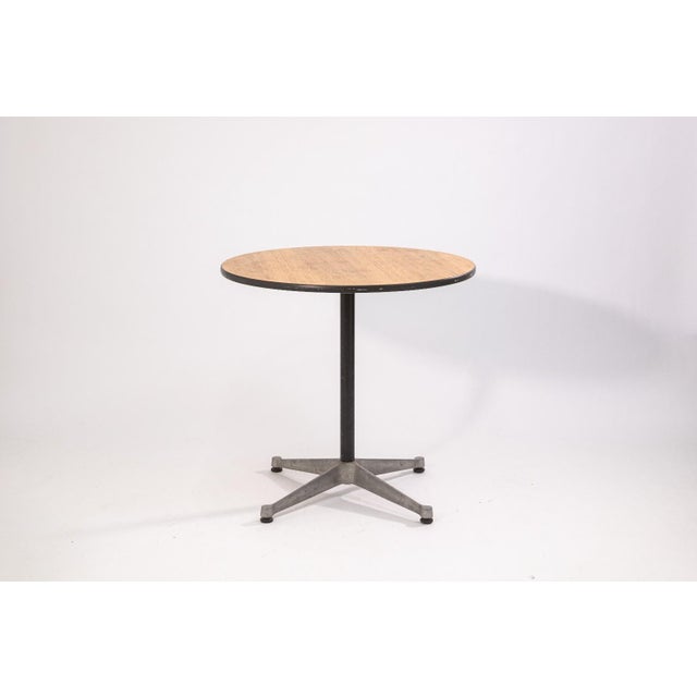 A Herman Miller round side table with wood top and metal base. The table features a circular wood surface with a...
