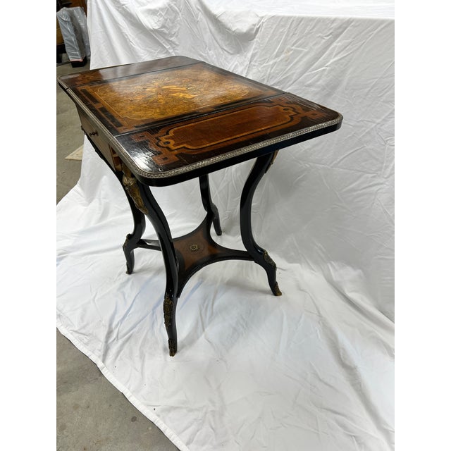 Antique late 19th century French style ebonized legs with gilt bronze mounts hold a one drawer, drop side top of marquetry...