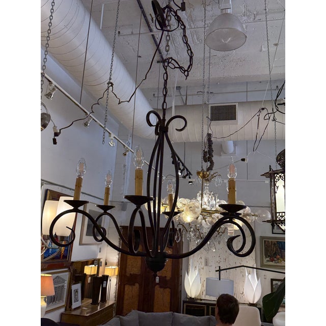 Design Plus Gallery presents a Scrolling Iron Like Chandelier. The frame is formed in black painted metal with sweeping...