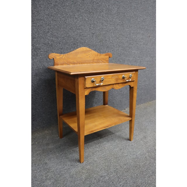 Oak nightstand attributed to American of Martinsville, featuring a clean, classic silhouette with a single drawer over an...