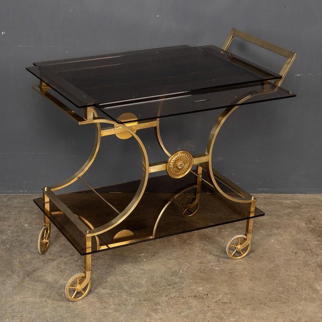 A mid 20th Century French brass bar cart with retractable sliding serving trays set with smoked glass, by a renowned...