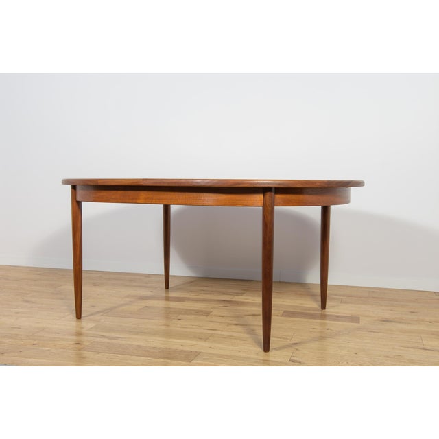 This is an oval-shaped teak dining table manufactured by G-Plan in the 1960s. The table has reinforced edges of the top....