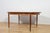 This is an oval-shaped teak dining table manufactured by G-Plan in the 1960s. The table has reinforced edges of the top....
