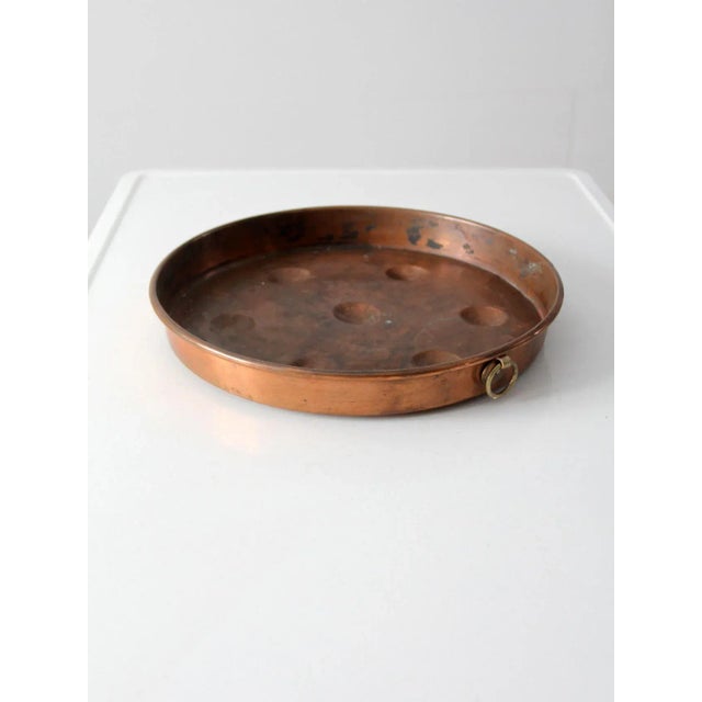An antique molded copper escargot pan featuring a classic round form with seven evenly spaced indentations designed for...