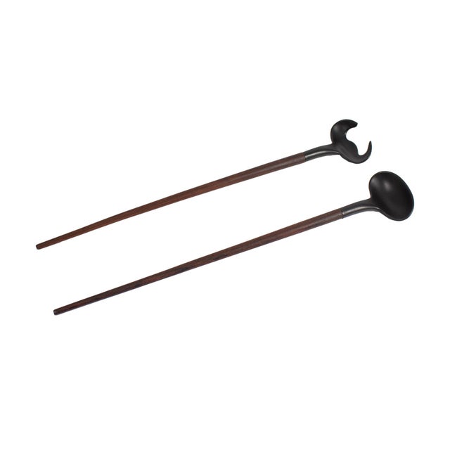 A pair of mid-century salad servers. Unmarked, the servers have black melamine tops and elongated wooden handles.